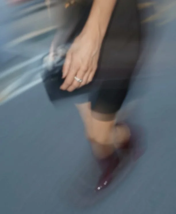 Motion-blurred street scene with a hand, silver ring and red shoes