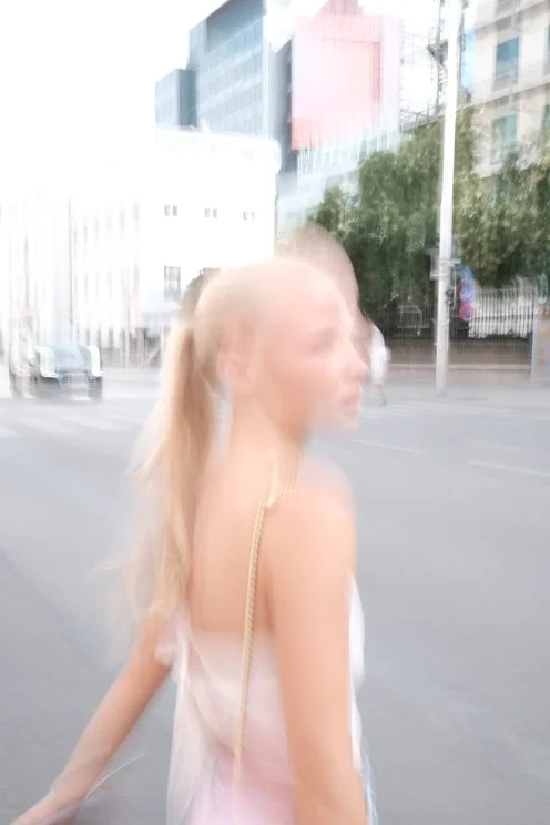 Louisa Reiter crossing a city street in bright light, hair in a ponytail
