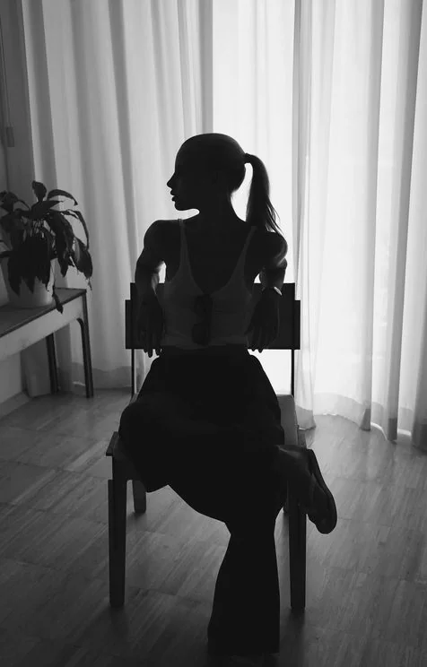 Silhouette of Louisa Reiter sitting on a chair in front of sheer curtains
