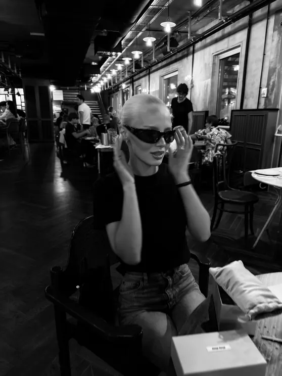 Black-and-white photo of Louisa Reiter adjusting her sunglasses at a restaurant table