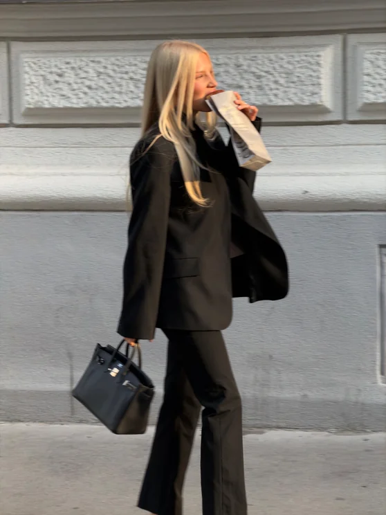 Louisa Reiter walking along a Vienna street in a black suit, carrying a handbag